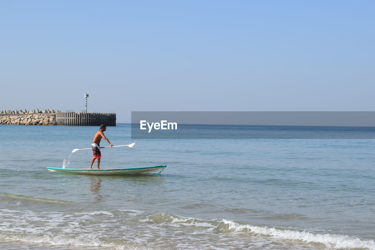 Man paddleboarding on sea against sky