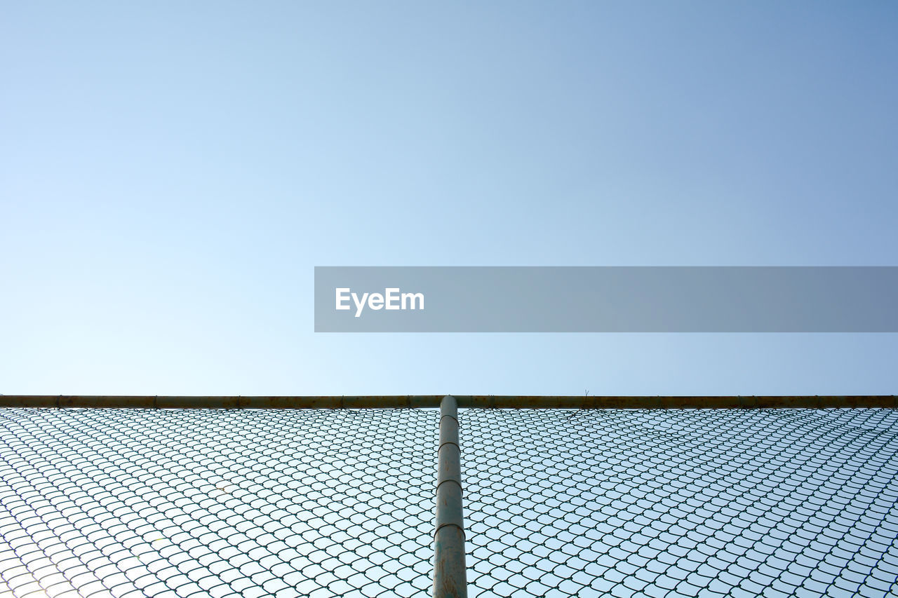 LOW ANGLE VIEW OF CHAINLINK FENCE AGAINST CLEAR BLUE SKY