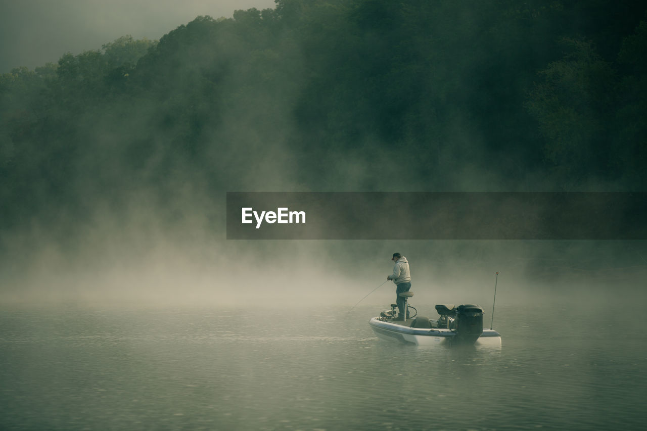 Rear view of man fishing at lake during foggy weather