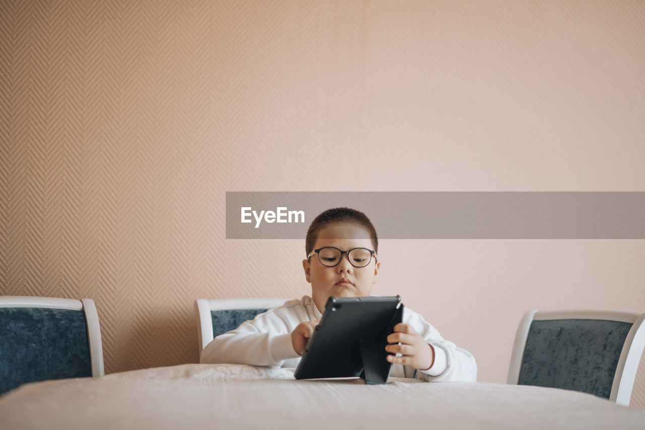 Boy in glasses is intently focused on tablet, suggesting moment of digital exploration