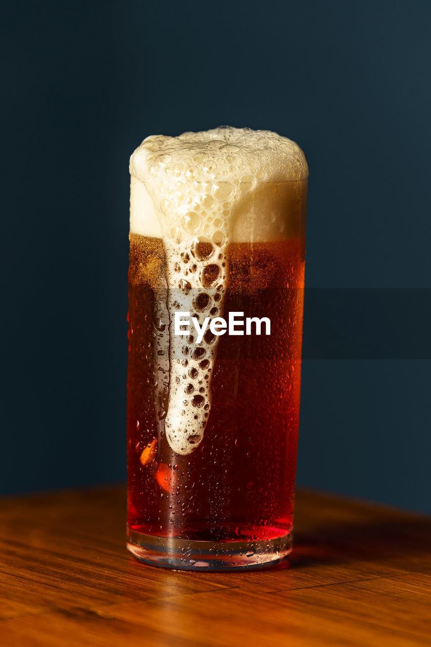CLOSE-UP OF BEER IN GLASS ON TABLE AGAINST BLACK BACKGROUND