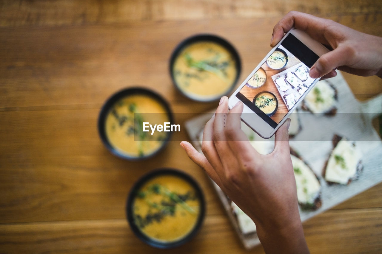 Hands of female blogger photographing pumpkin soup and crispbread through smart phone at creative office