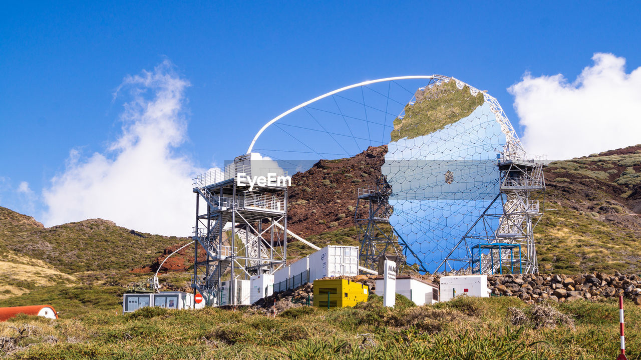 Incomplete satellite dish on field against sky