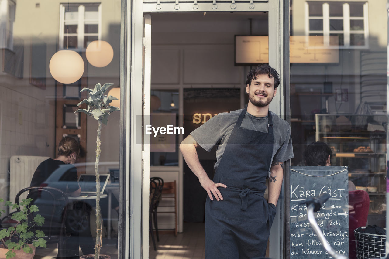 Portrait of smiling male entrepreneur leaning while standing at cafe entrance