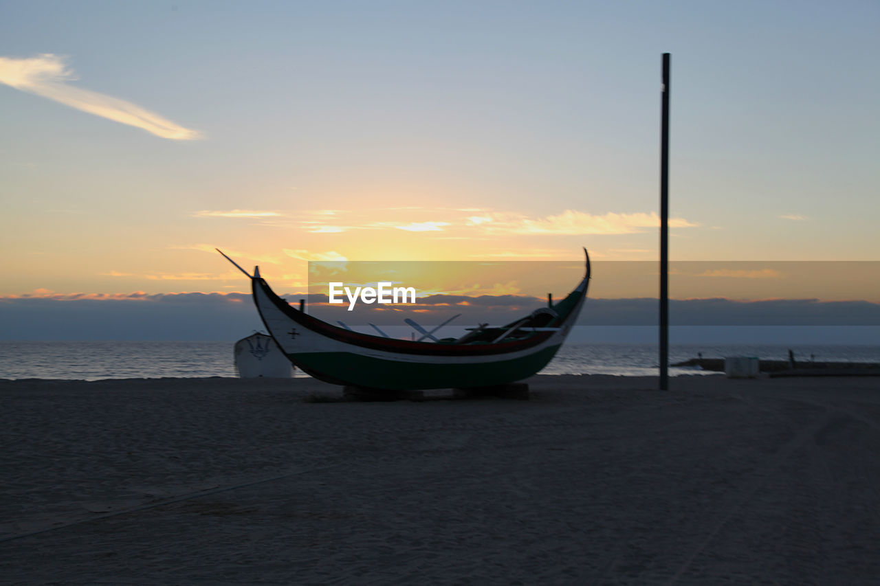 BOAT MOORED ON BEACH AGAINST SKY AT SUNSET