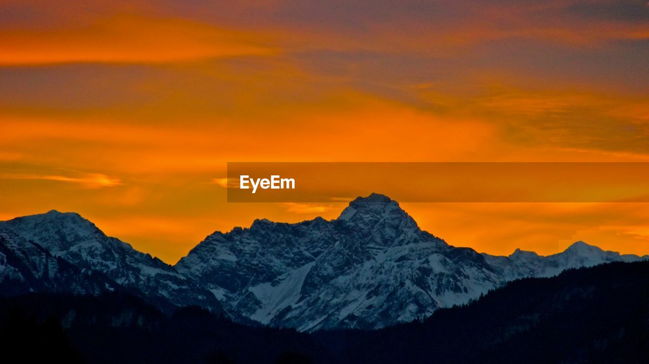 Scenic view of snowcapped mountains against orange sky