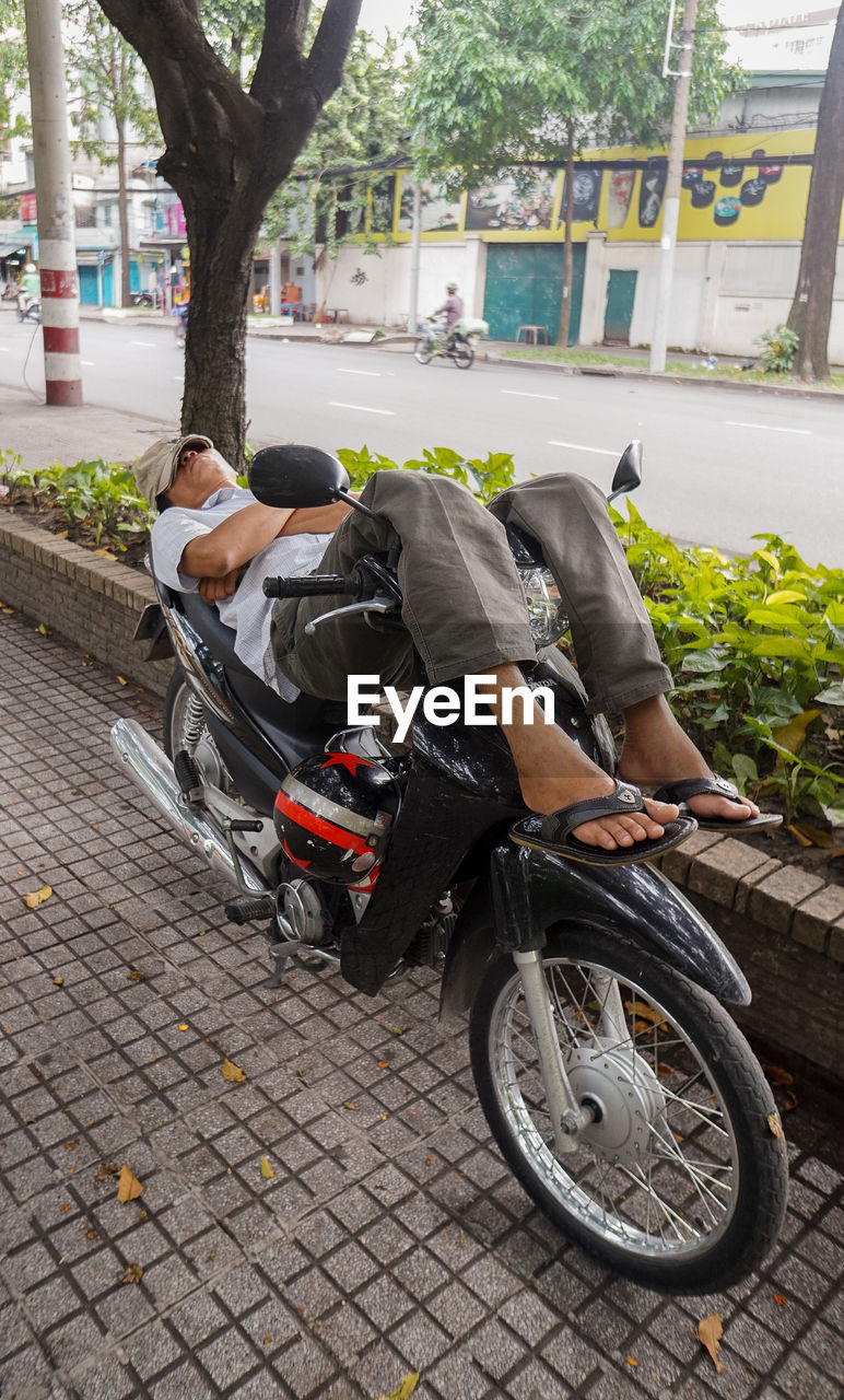 Man relaxing on motor scooter at sidewalk