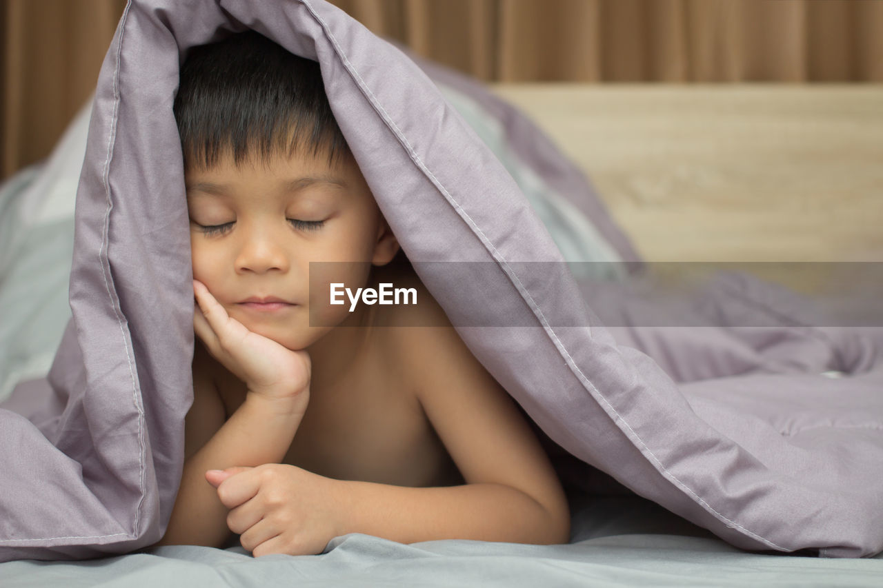 Close-up of boy sleeping with blanket on bed