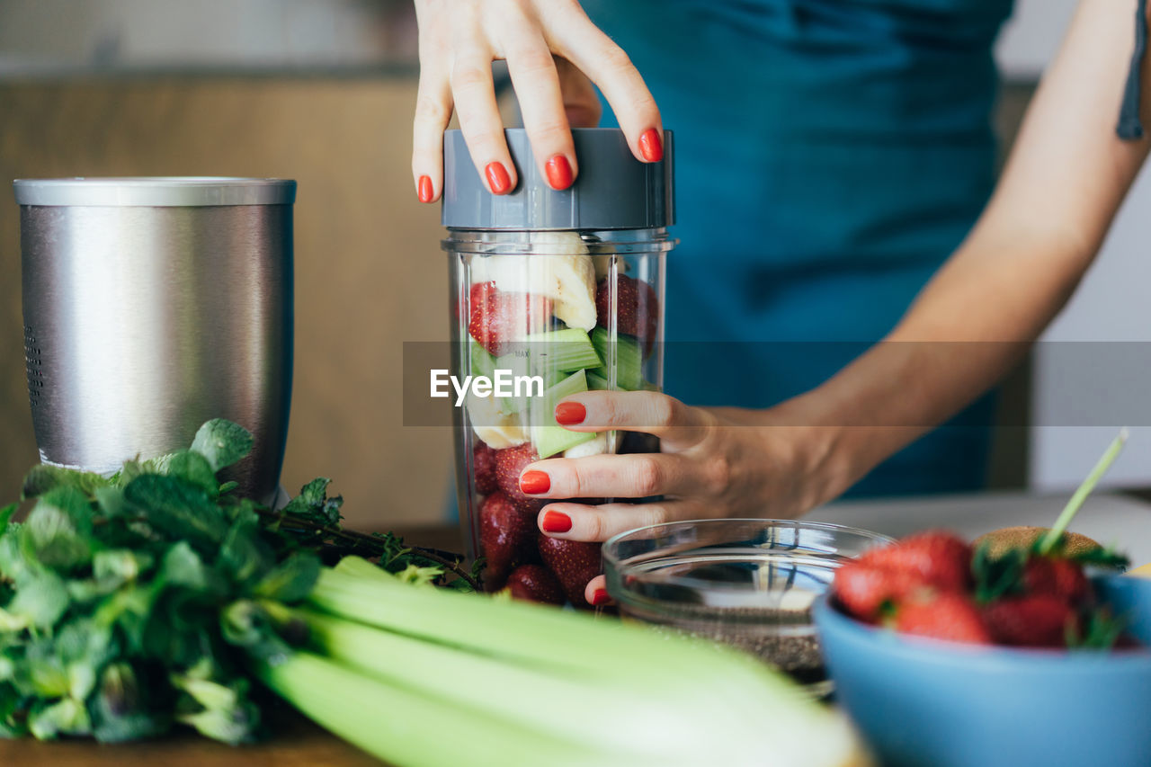 Female hands close the lid of the blender bowl with strawberry, banana and celery. 