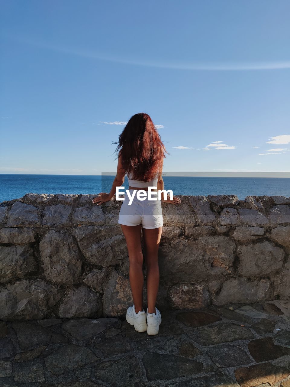 Rear view of woman standing by sea against sky