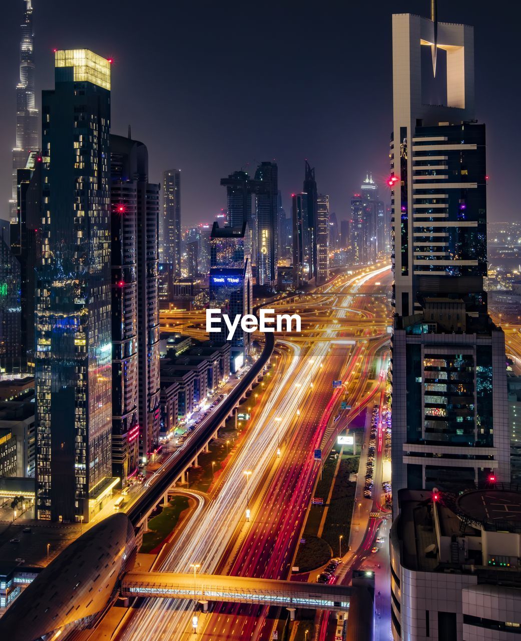 High angle view of light trails on road amidst modern buildings against sky at night