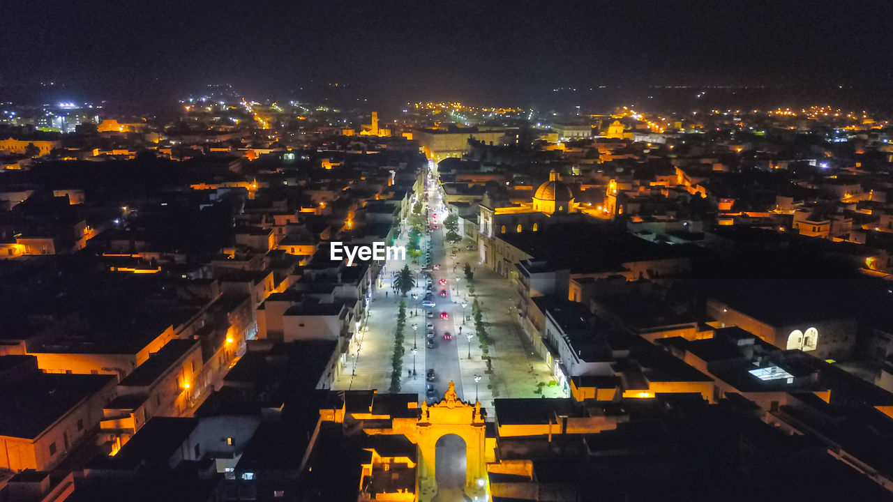 HIGH ANGLE VIEW OF ILLUMINATED STREET AMIDST BUILDINGS AT NIGHT