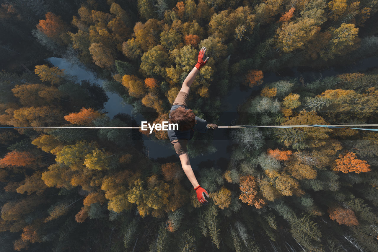 A breathtaking view of a tightrope walker walking along a line high above a beautiful forest.