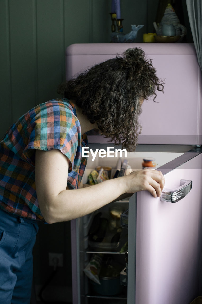 Side view of woman opening door of refrigerator in kitchen