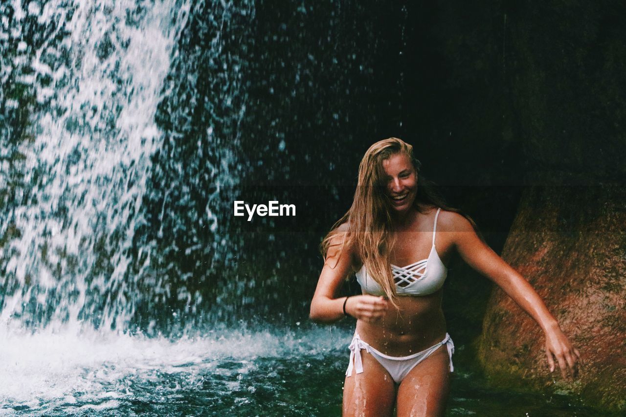 Young woman in bikini standing against waterfall