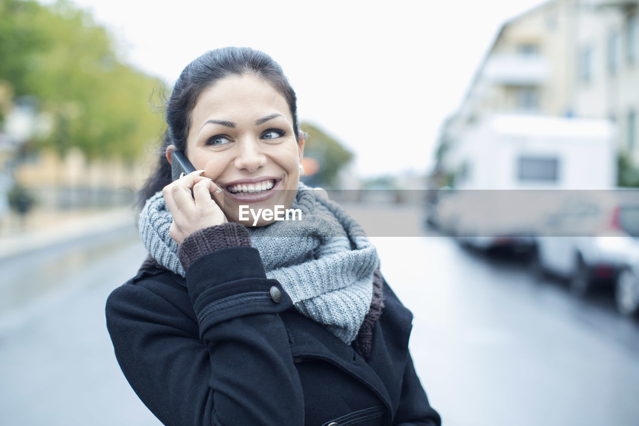 Smiling mid adult woman talking on smart phone on street