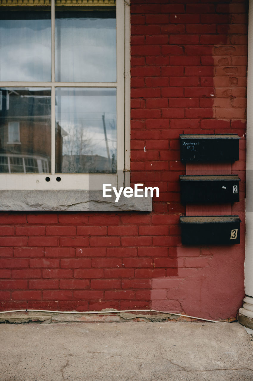 Stack of 3 mailboxes on red brick wall.