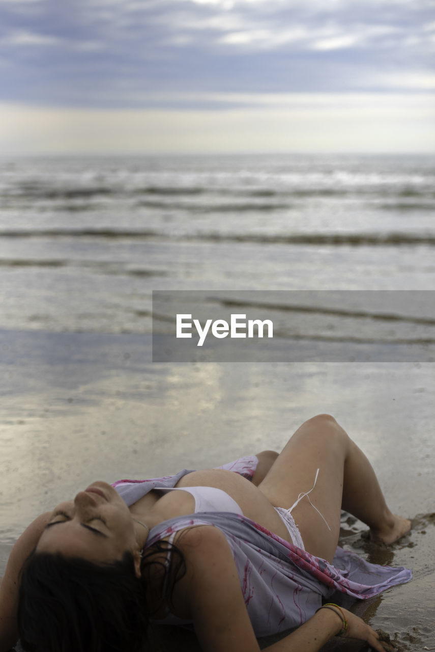 Woman relaxing on beach against sky