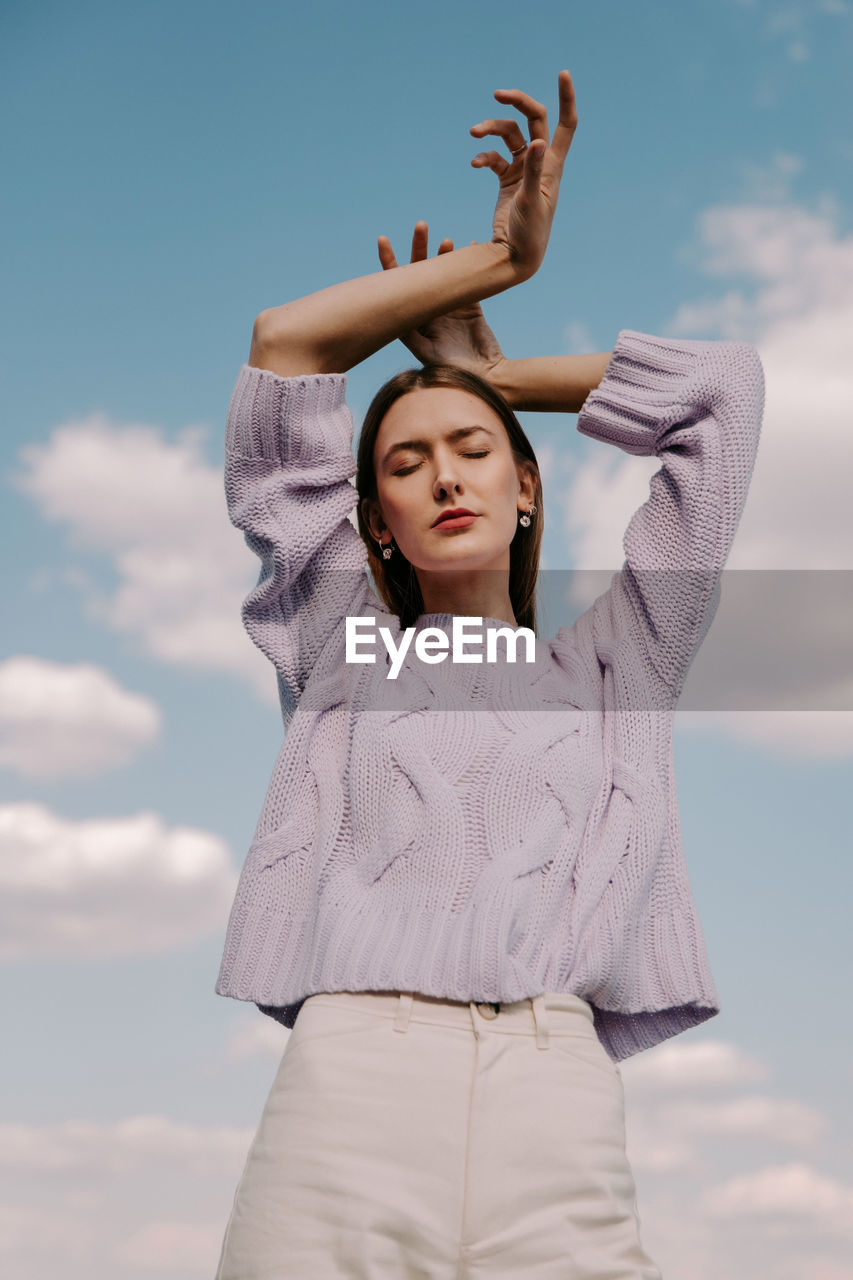 Young woman with arms raised standing against sky