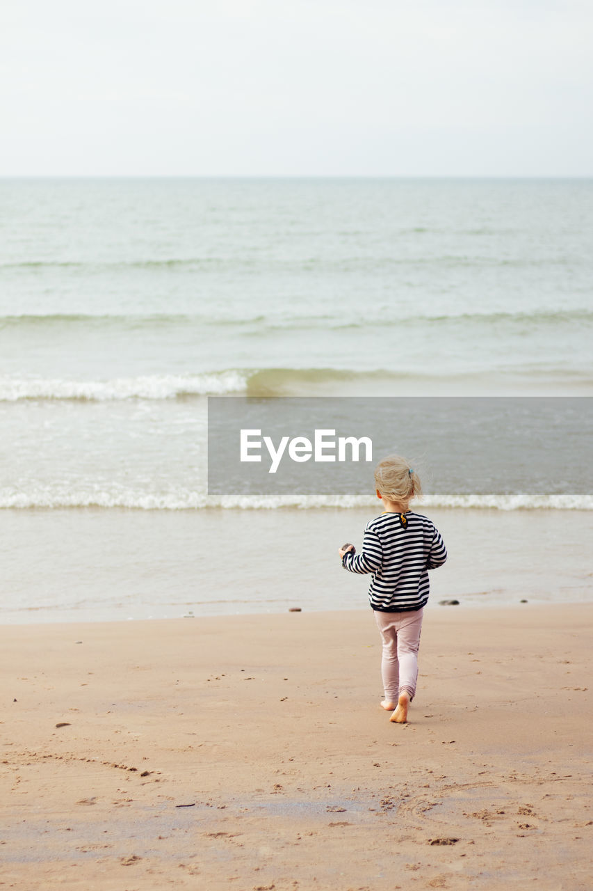 Rear view of girl walking at beach against clear sky