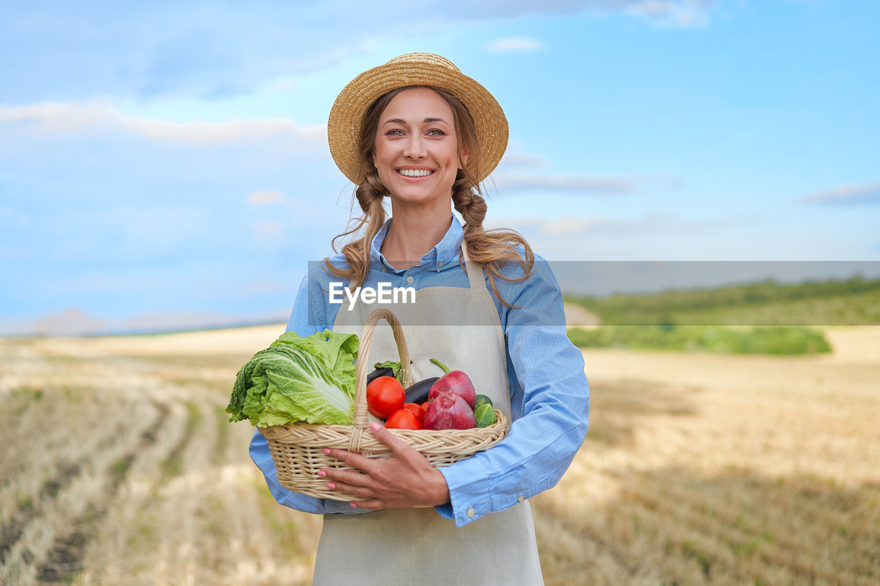 PORTRAIT OF SMILING YOUNG WOMAN STANDING ON WICKER BASKET