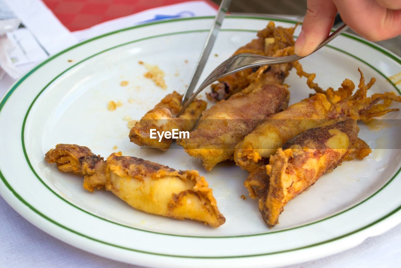 Cropped image of fingers cutting cooked squid