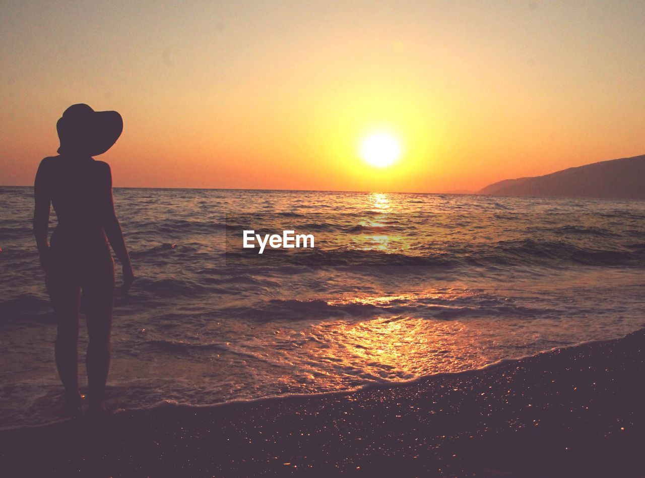 SILHOUETTE BOY STANDING ON BEACH DURING SUNSET