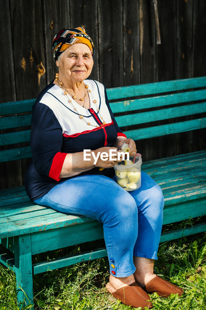 Senior woman peeling apple while sitting on bench at park