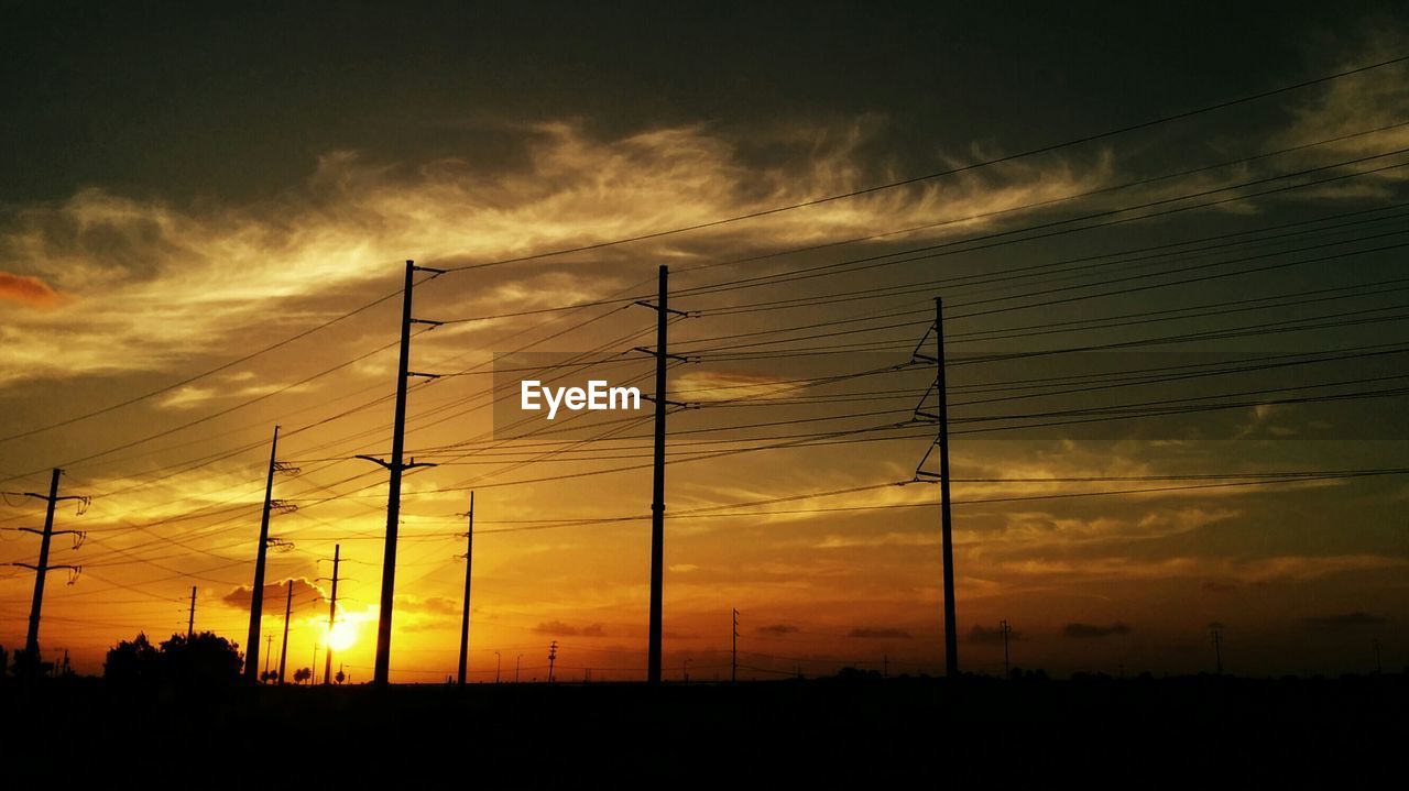 Low angle view of silhouette electricity pylons at sunset