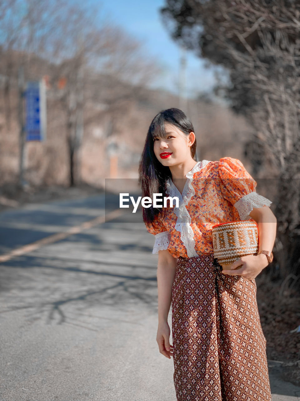 YOUNG WOMAN LOOKING AWAY WHILE STANDING AGAINST BLURRED BACKGROUND