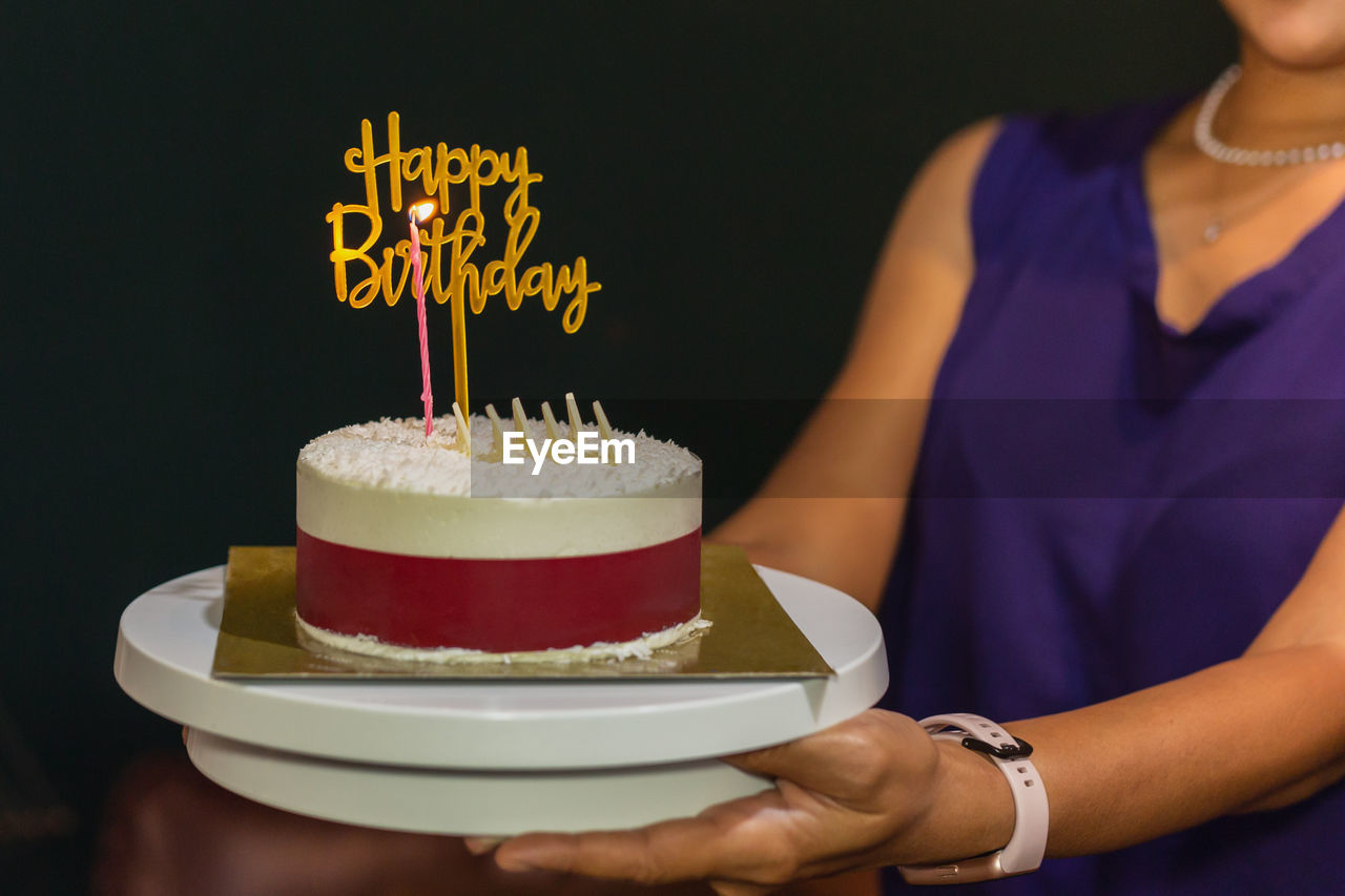 Woman holding birthday cake with candle and birthday plate.