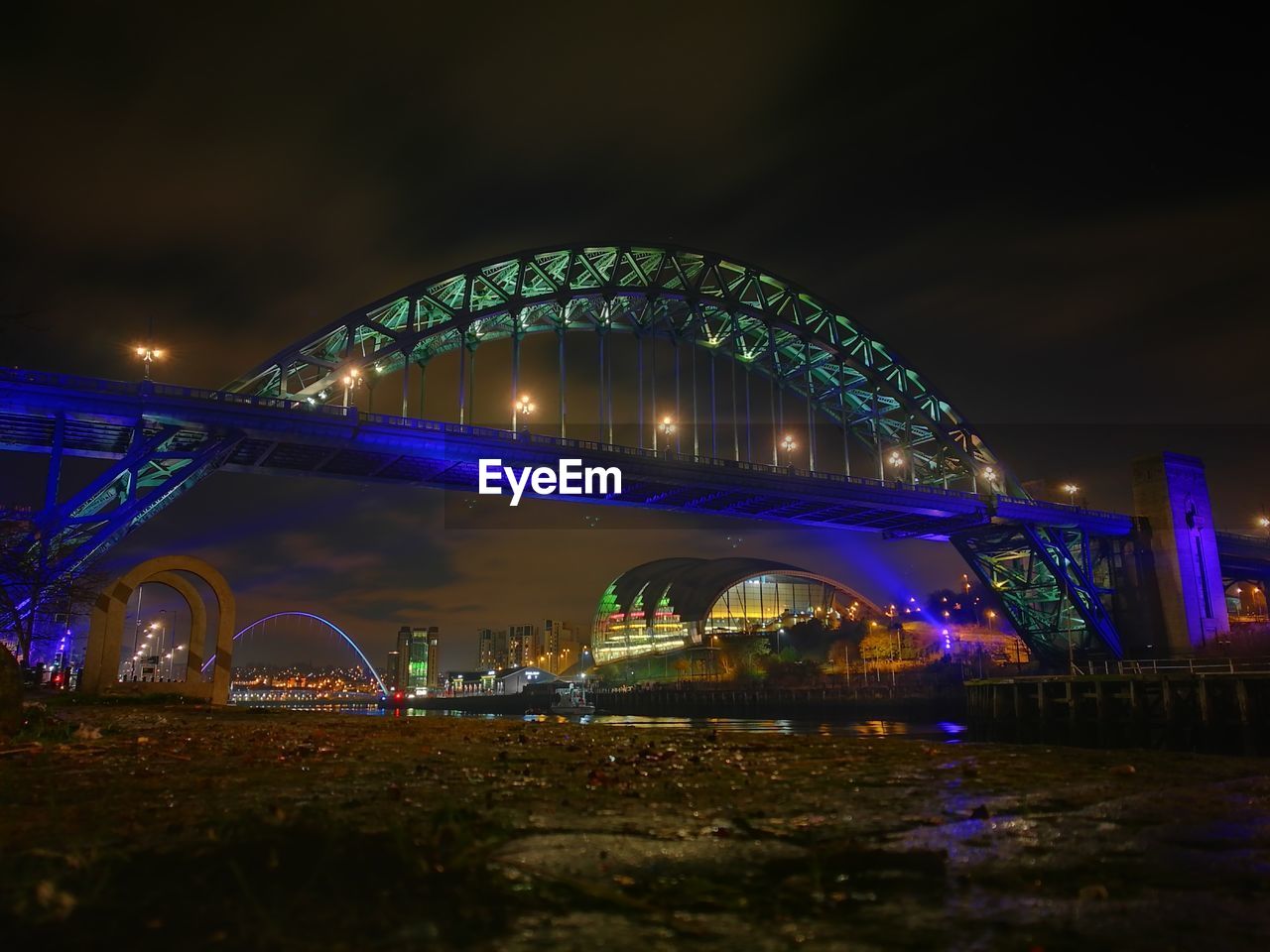 ILLUMINATED BRIDGE OVER RIVER IN CITY AT NIGHT