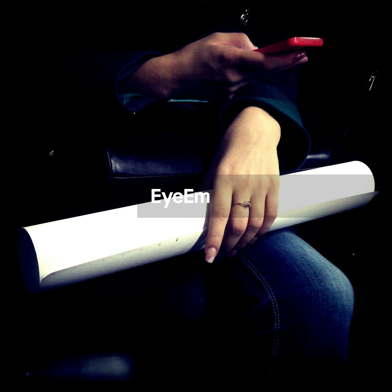 Midsection of woman using mobile phone while holding rolled up paper