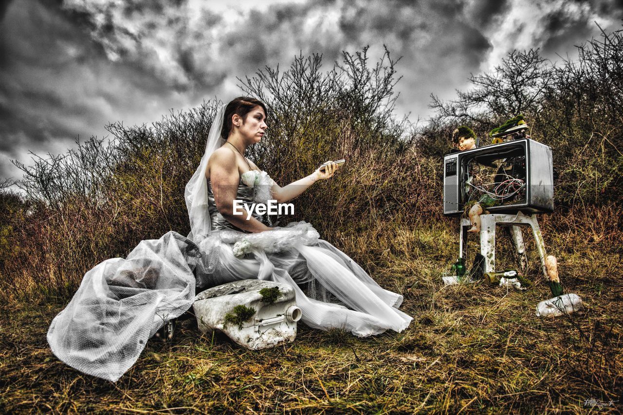 Bride watching television while sitting on field 