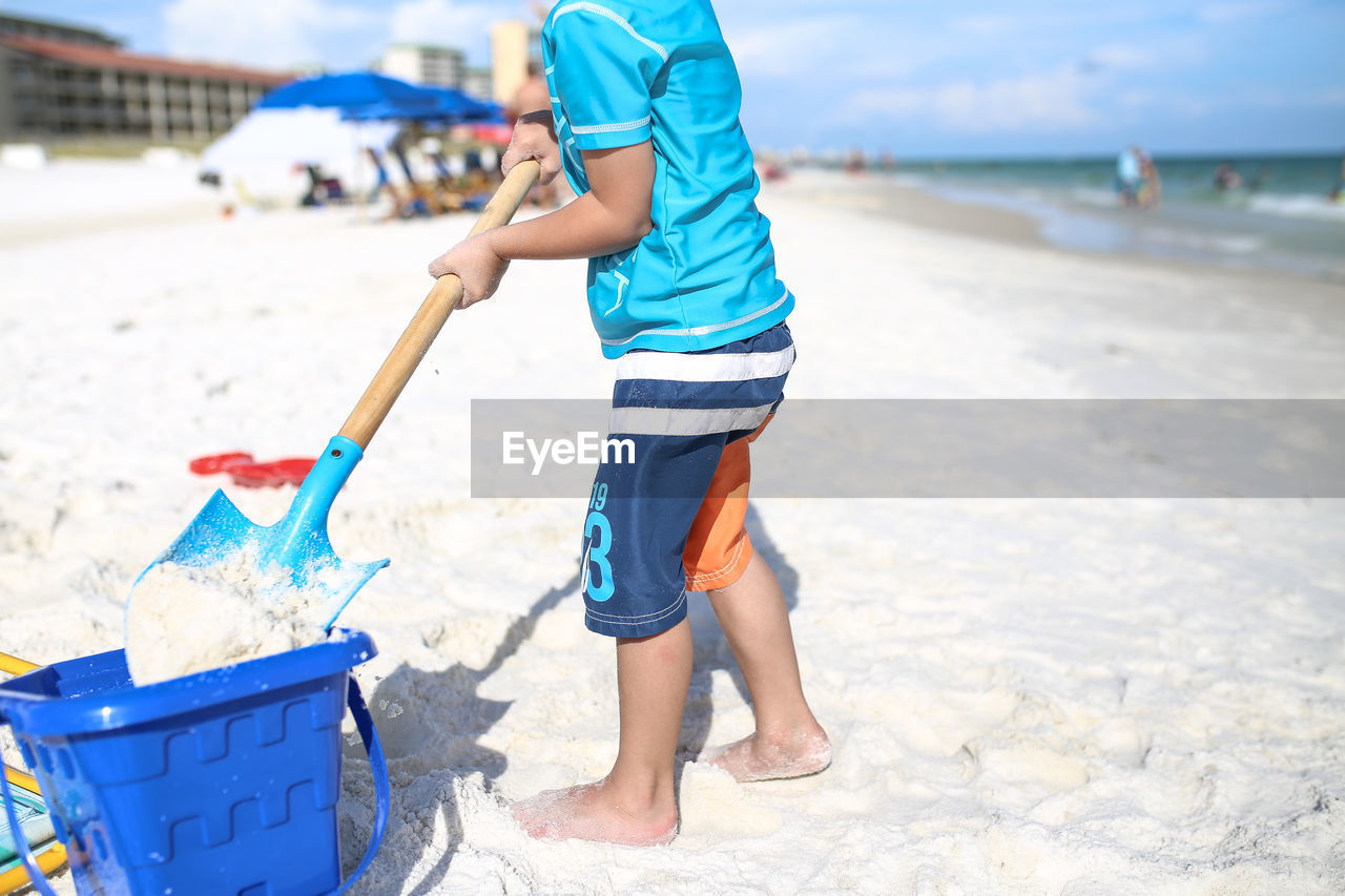 Low section of boy digging sand at beach