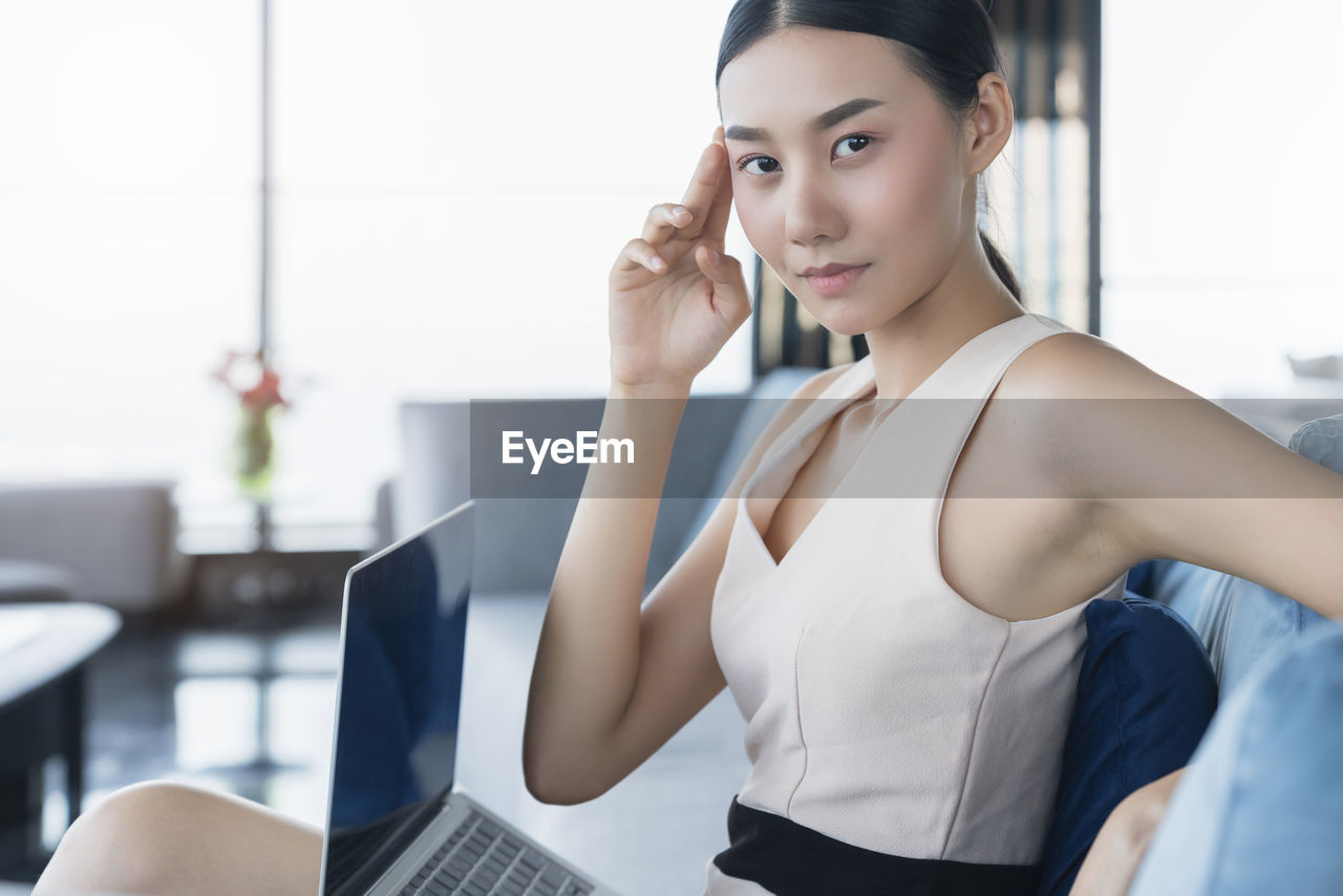 PORTRAIT OF YOUNG WOMAN USING MOBILE PHONE IN OFFICE