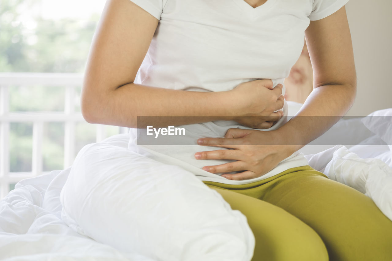 Midsection of woman with stomachache kneeling on bed at home