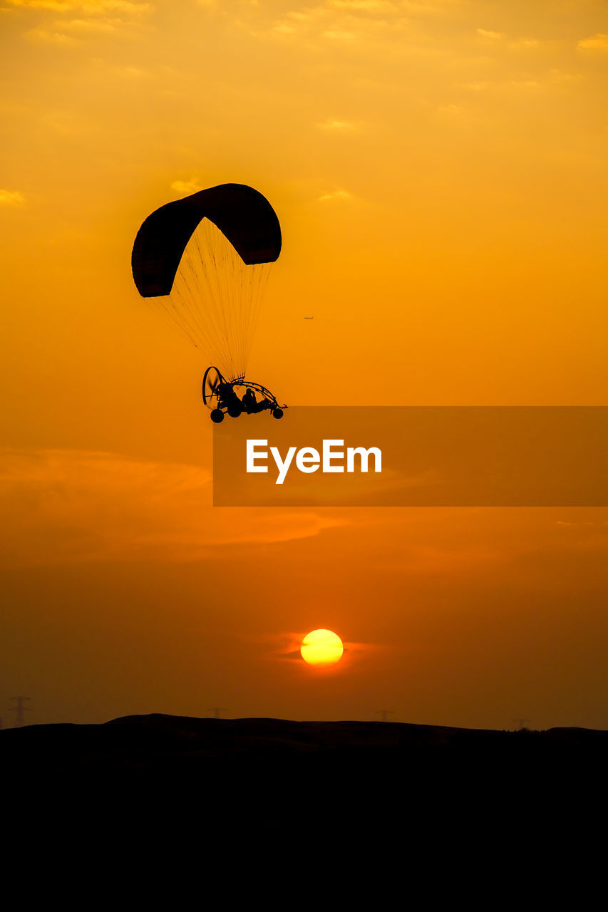 silhouette people paragliding against orange sky