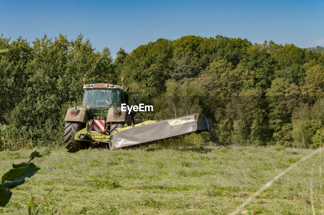 TRACTOR ON FIELD AGAINST TREES