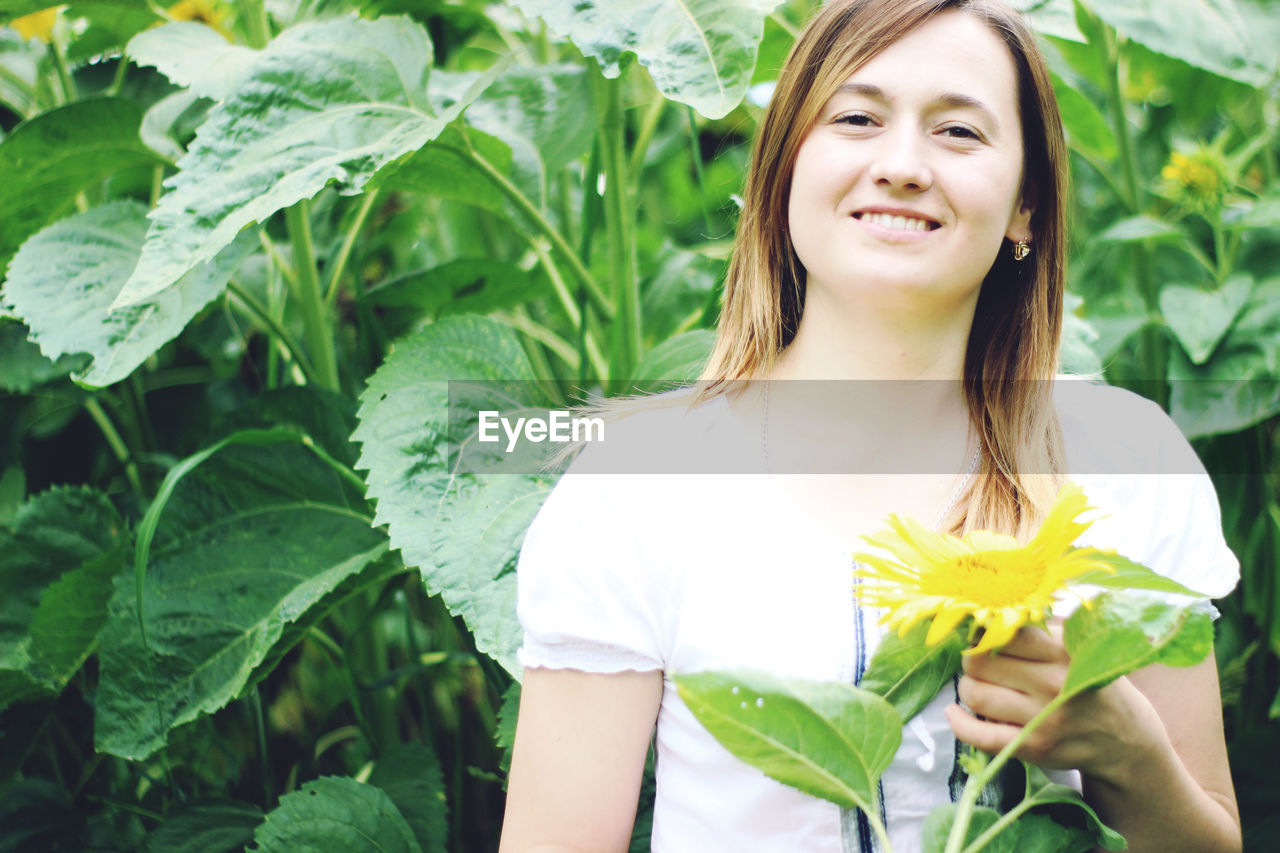 Portrait of young woman standing against sunflower plants on field