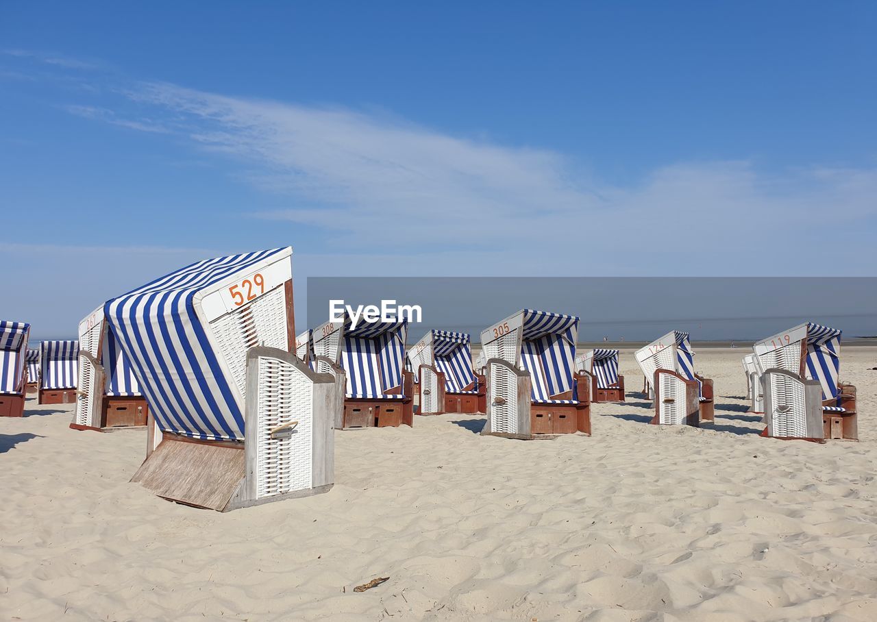 Hooded chairs on beach against sky at norderney, germany