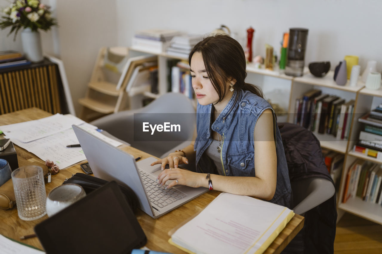 Young woman using laptop while doing school assignment at home