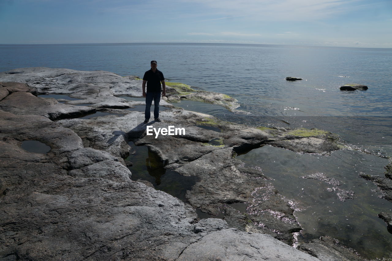 water, sea, sky, one person, coast, shore, rock, ocean, beauty in nature, full length, nature, scenics - nature, horizon over water, leisure activity, horizon, beach, land, cliff, lifestyles, standing, tranquility, men, rear view, tranquil scene, day, adult, terrain, non-urban scene, holiday, body of water, wave, idyllic, vacation, outdoors, cloud, bay, trip, activity, solitude