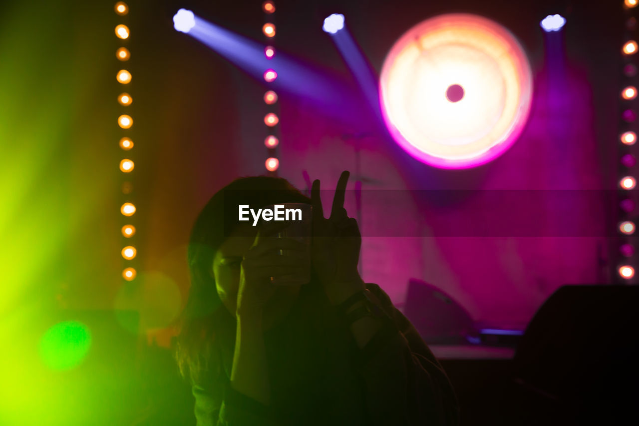 Woman gesturing while holding drink at illuminated nightclub