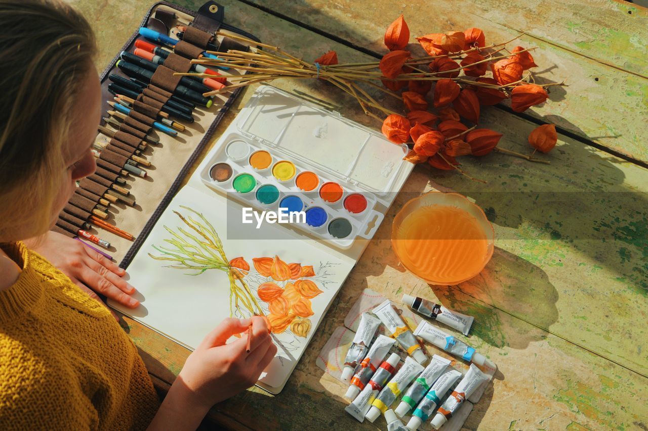 High angle view of female artist painting flowers in notebook