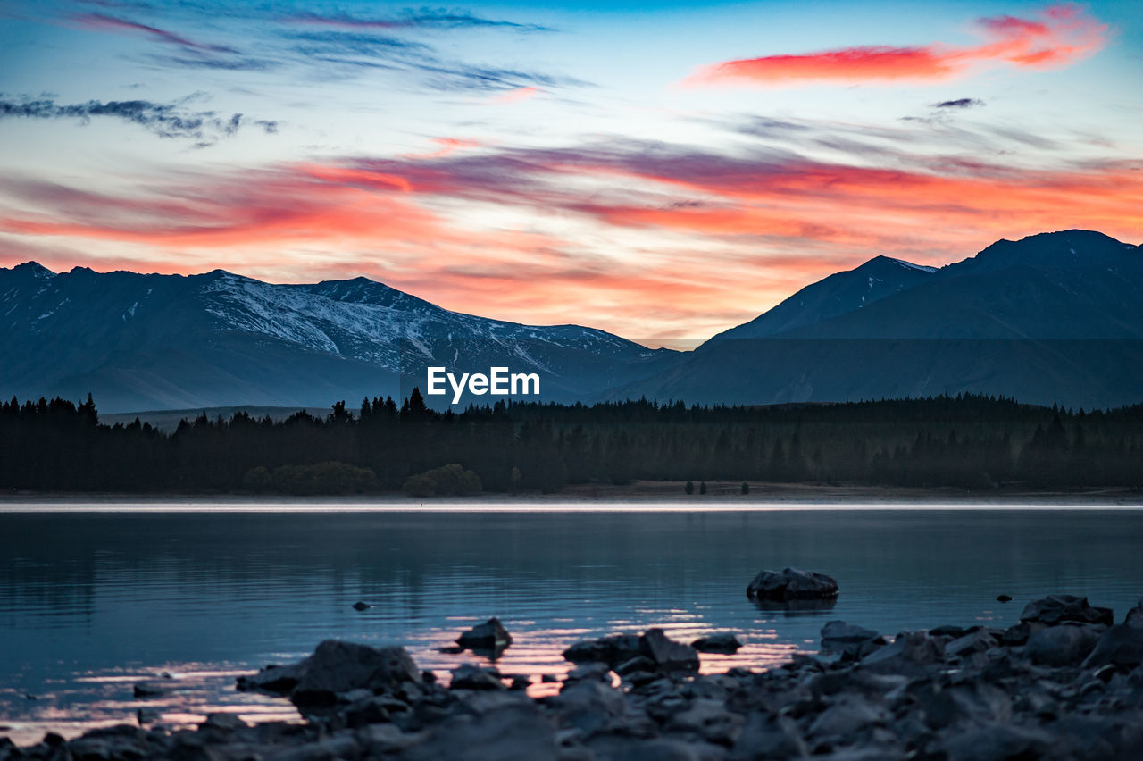 Scenic view of lake by mountains against sky during sunset