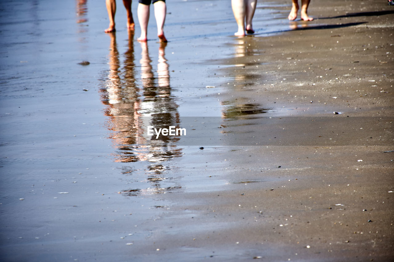 PEOPLE WALKING ON WET BEACH