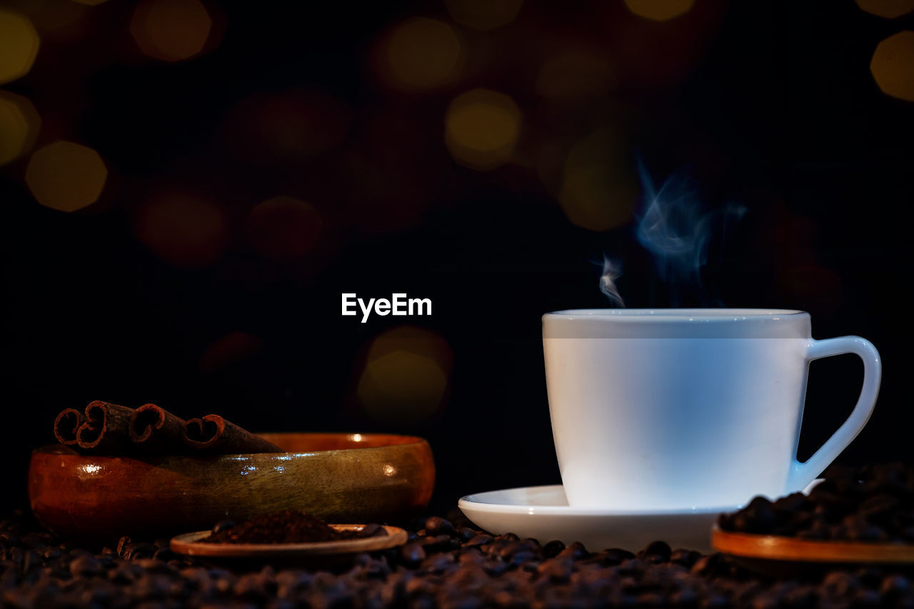 CLOSE-UP OF COFFEE CUP ON TABLE AT ILLUMINATED CAFE