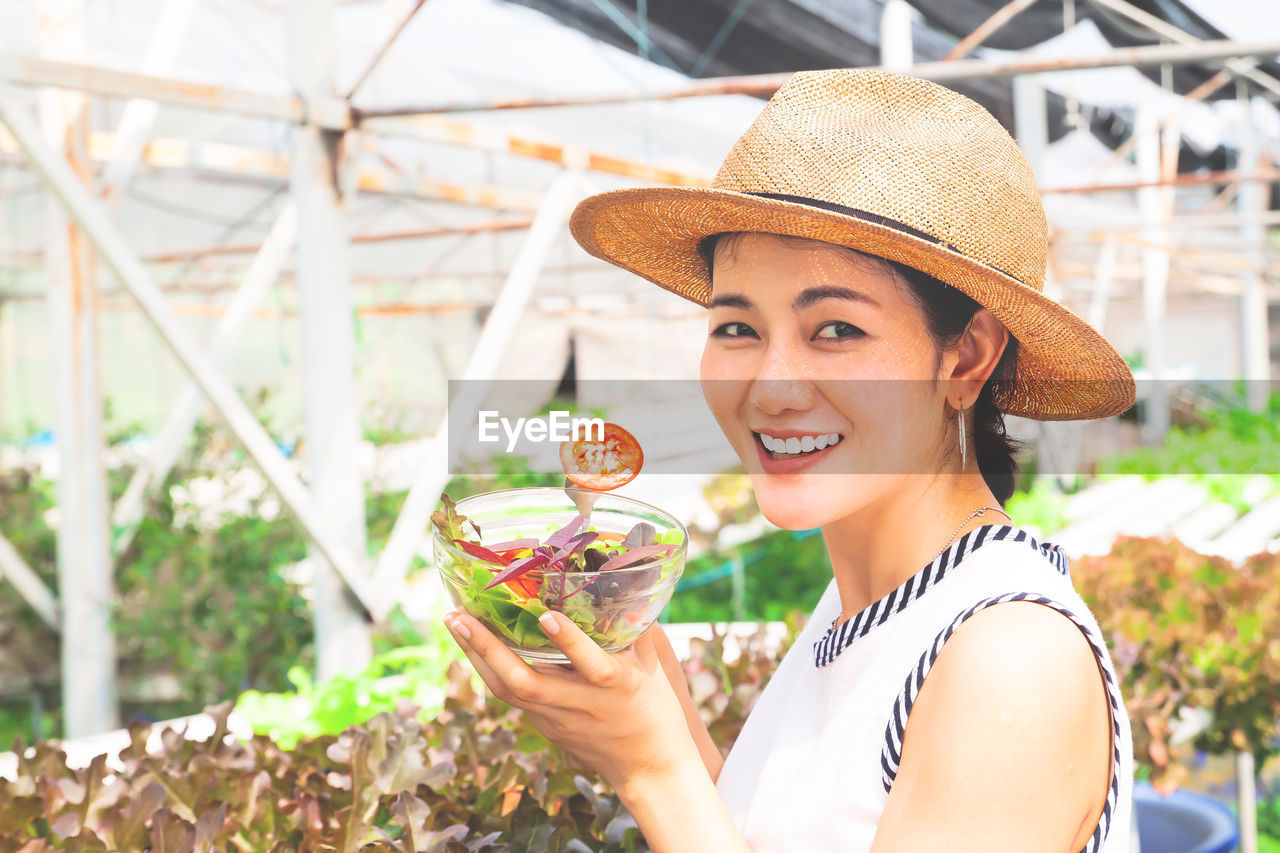 Portrait of smiling woman holding salad bowl in greenhouse