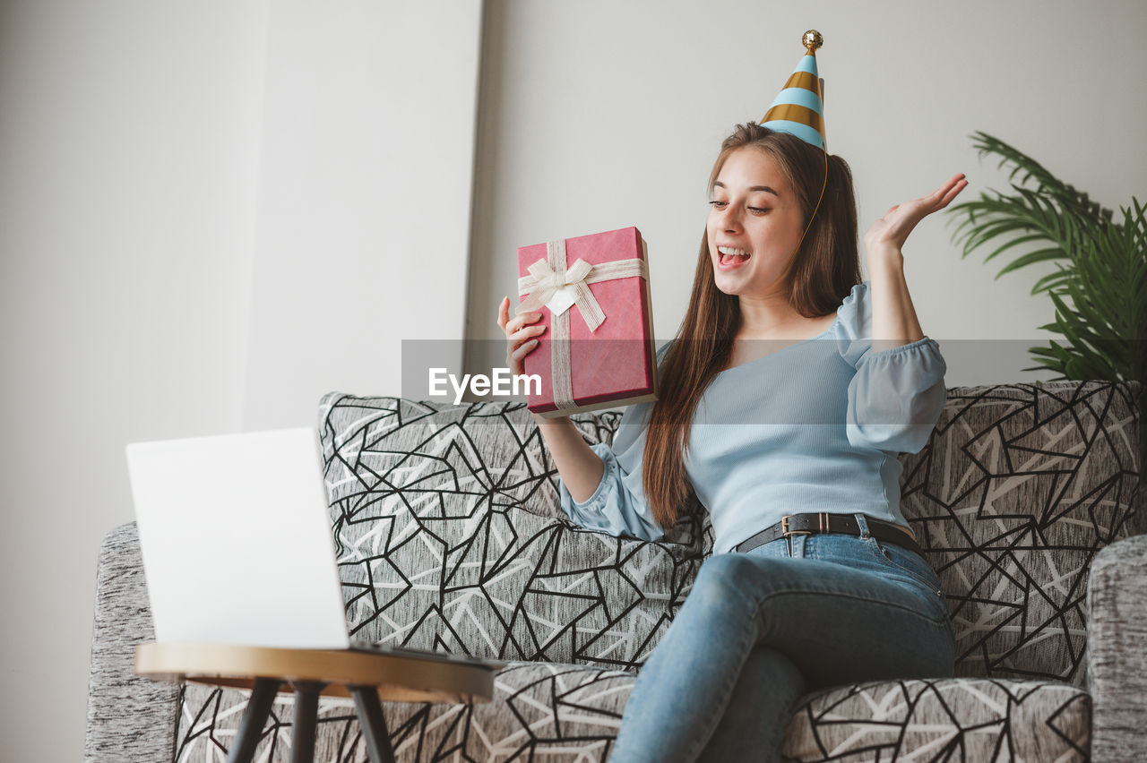 YOUNG WOMAN SMILING WHILE SITTING ON SOFA